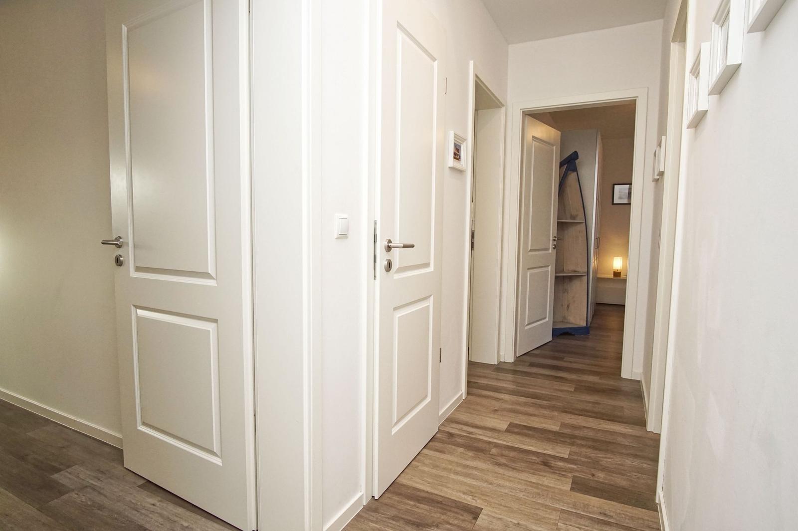 Flur mit weißen Türen und Holzboden. Im Hintergrund ist ein weiterer Raum sichtbar.