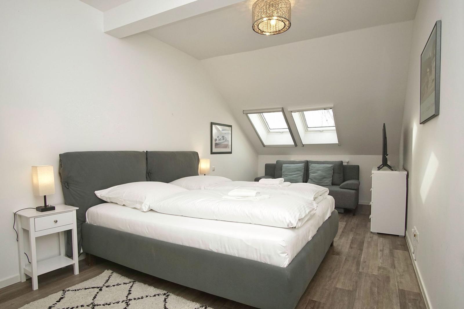 Schlafzimmer mit Doppelbett, Sitzgelegenheit und Dachfenstern.