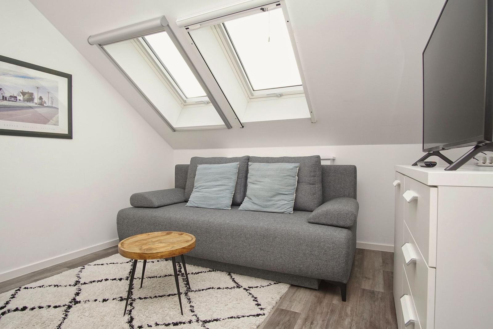 Wohnzimmer mit grauem Sofa, Holztisch und Dachfenstern.