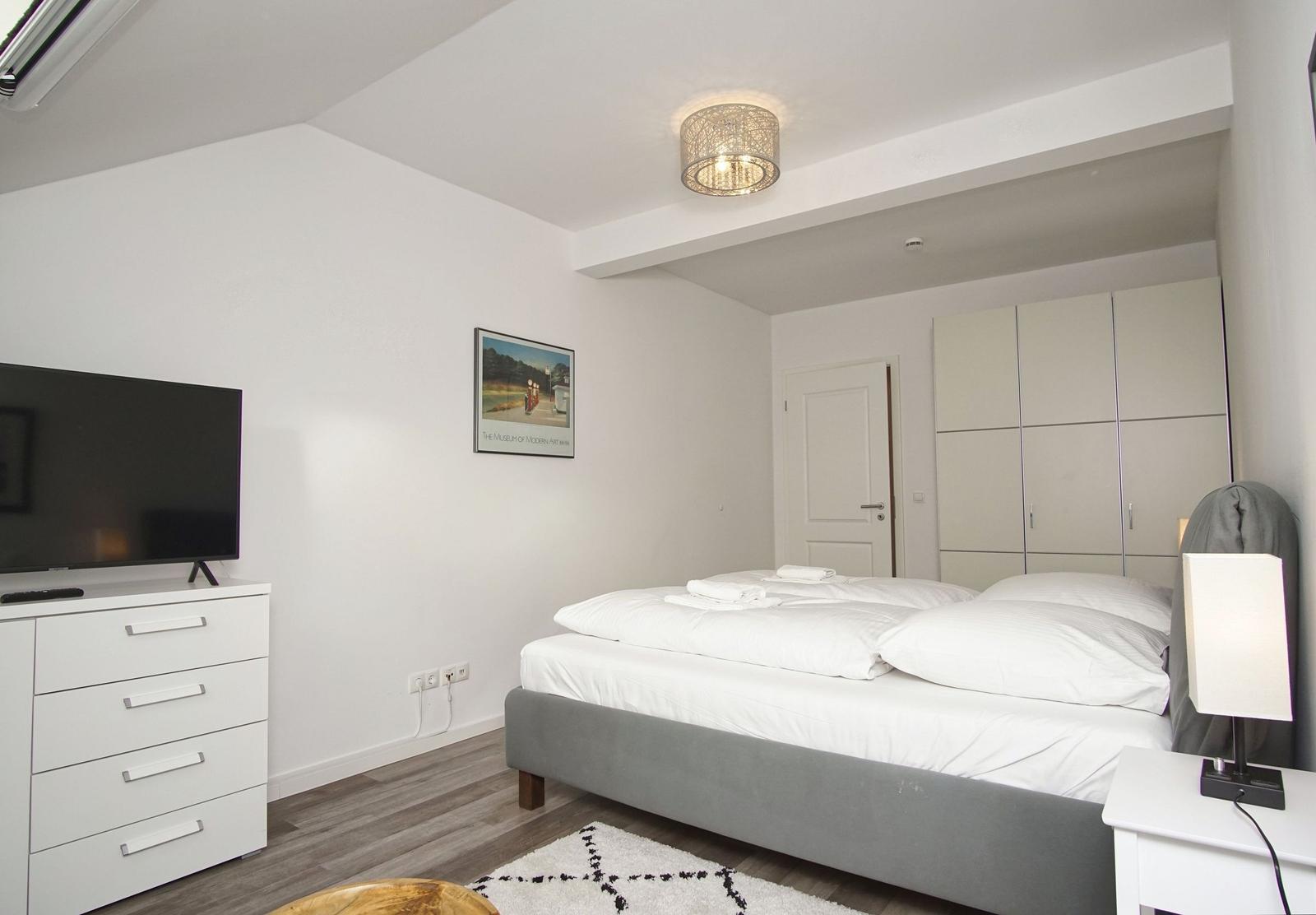 Schlafzimmer mit Bett, Kleiderschrank, Fernseher und Nachttisch.