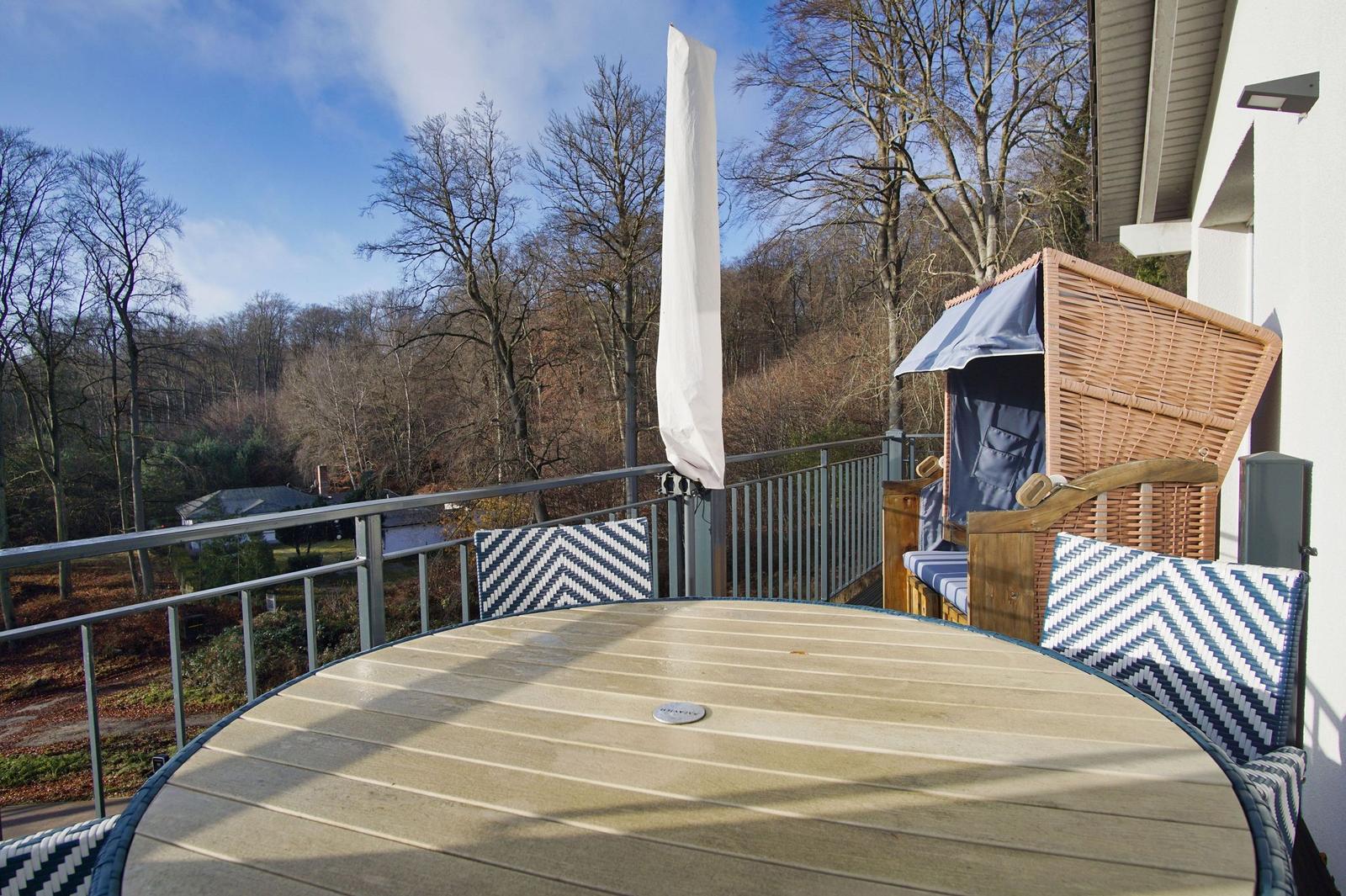 Terrasse mit Tisch, Stühlen und Strandkorb. Blick auf Wald und Himmel.