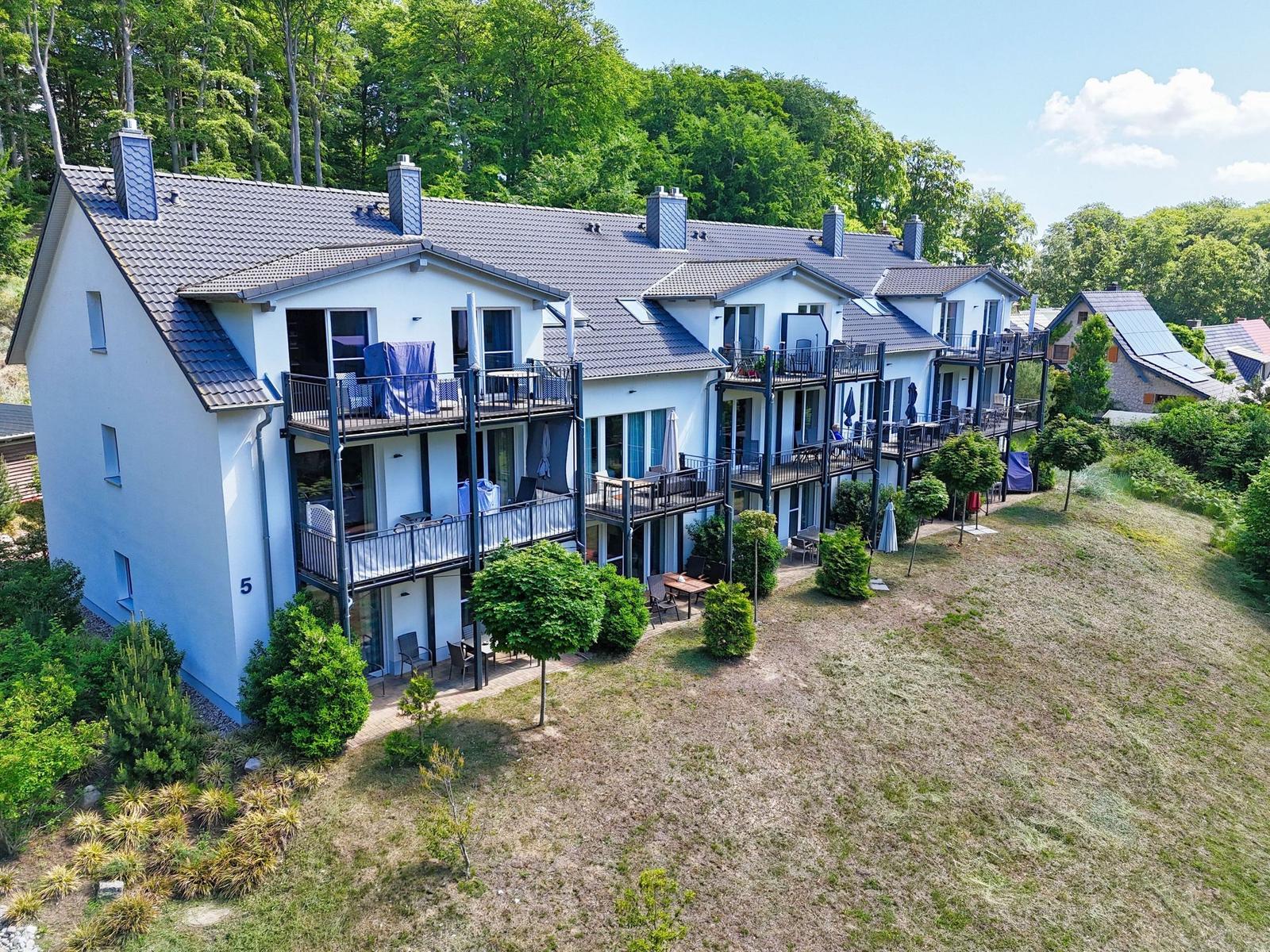Ferienhaus mit Balkonen und Garten. Umgeben von Bäumen und Grünflächen.
