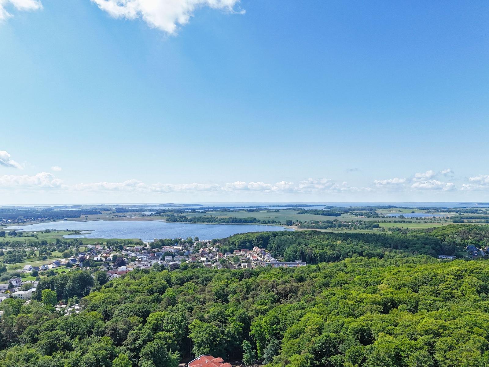 Panoramablick auf See, Wald und Dorf unter blauem Himmel mit weißen Wolken.