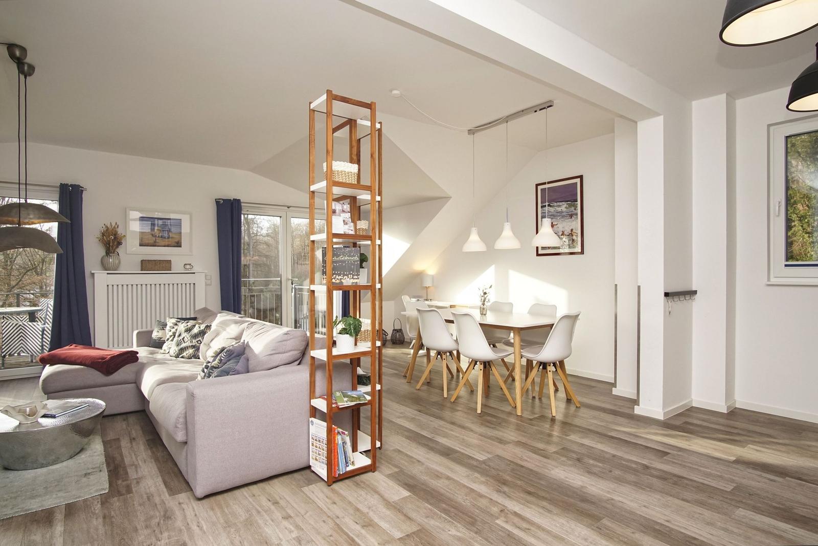 Wohn- und Essbereich mit Sofa, Tisch und Stühlen. Holzfußboden und Fenster.