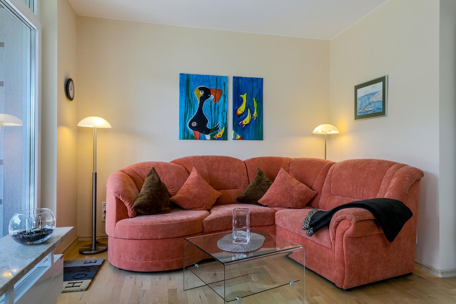 Ein Wohnzimmer mit einem roten Sofa, Glas-Tisch und Wandbildern.