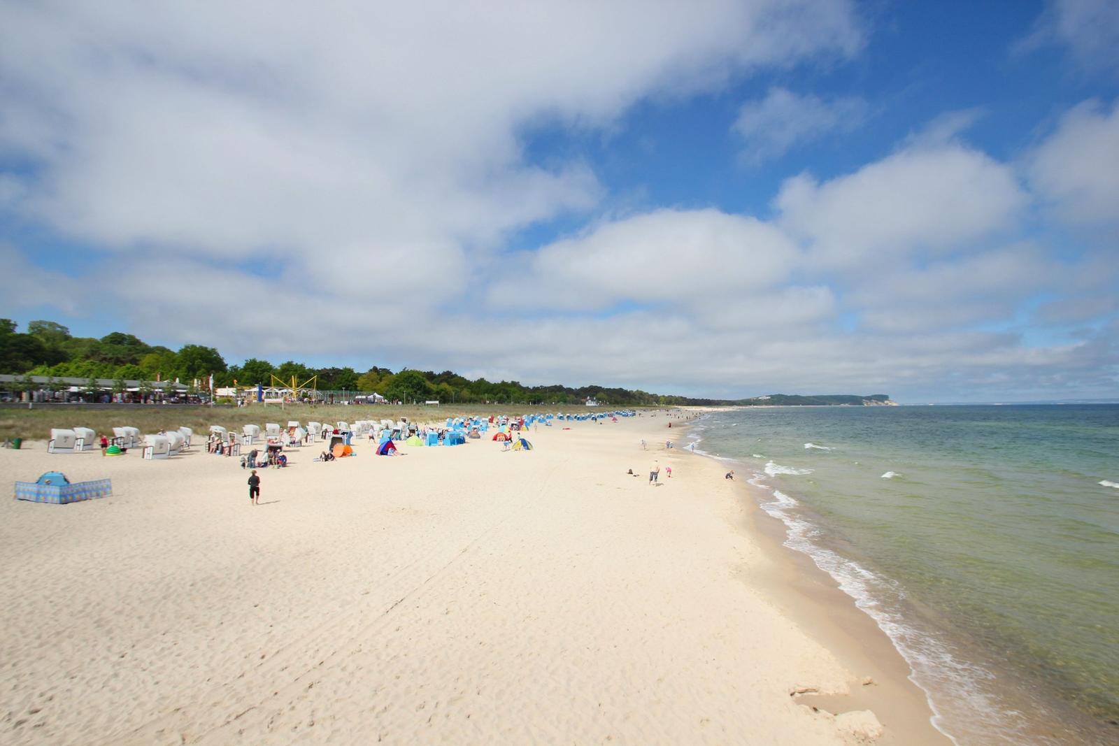 Strand mit weißen Sand, Wellen und bunten Strandkörben unter blauem Himmel.