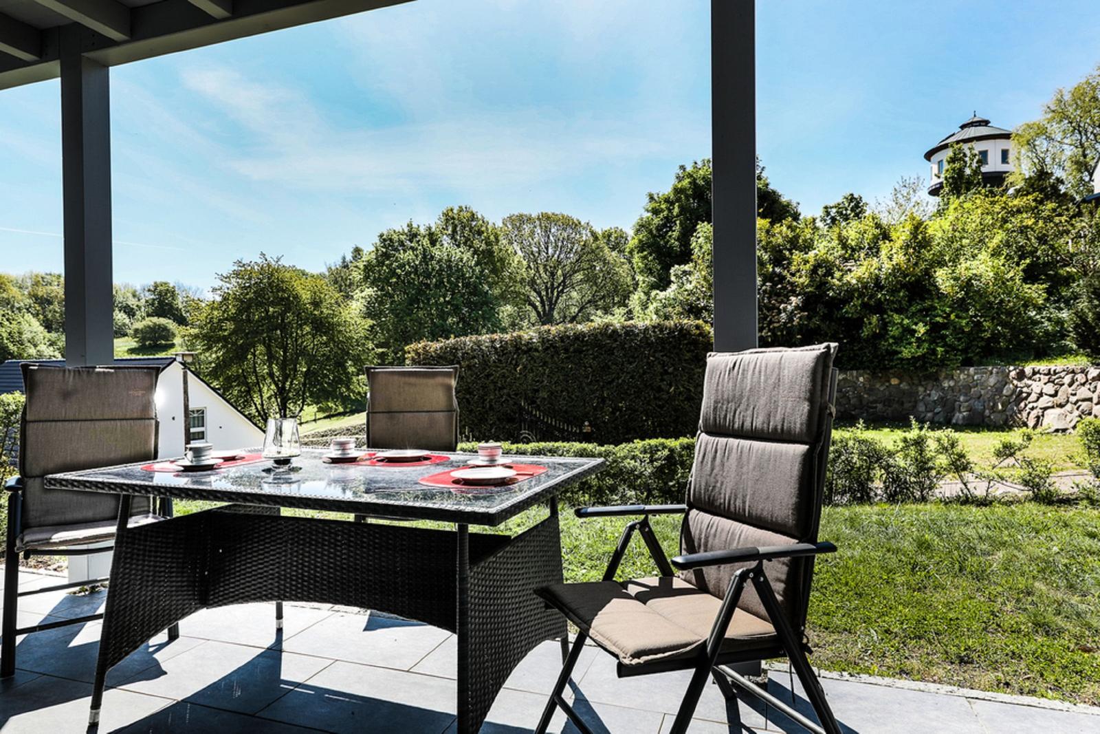 Terrasse mit Tisch und Stühlen. Blick auf grüne Bäume und einen Turm.