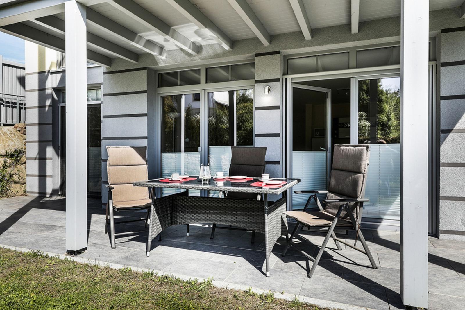 Terrasse mit Sitzgruppe, Tisch und Glashaus. Außenbereich mit Sonnenschutz.