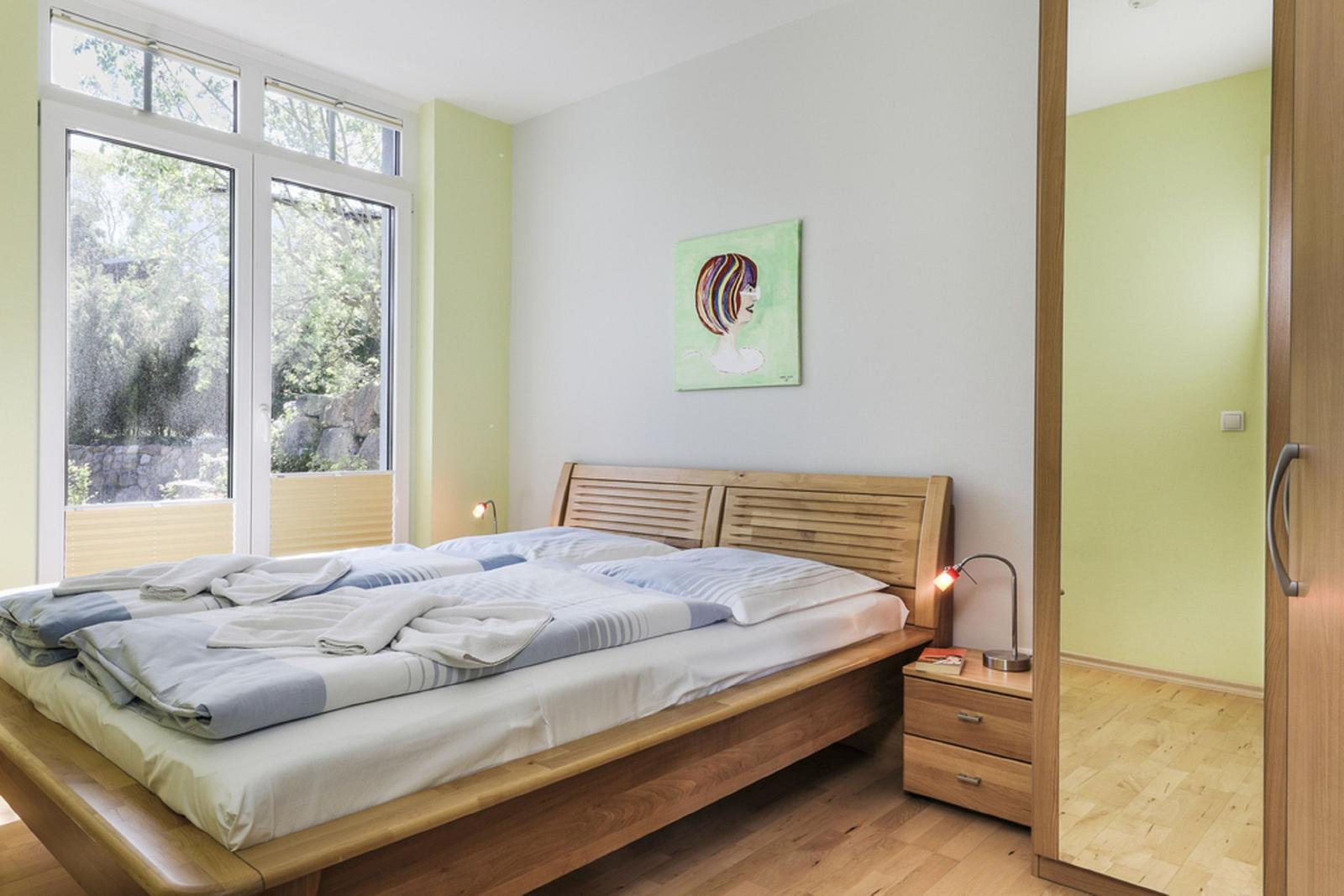 Schlafzimmer mit Holzbett, Fenster und Wandbild.