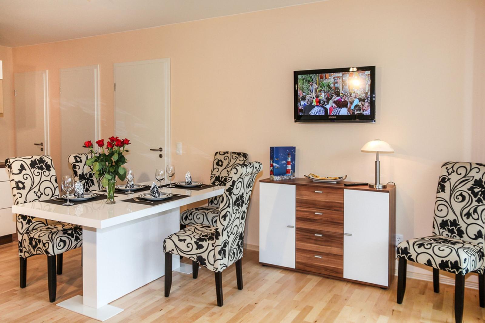 Essbereich mit Tisch, Stühlen und Fernseher an der Wand.