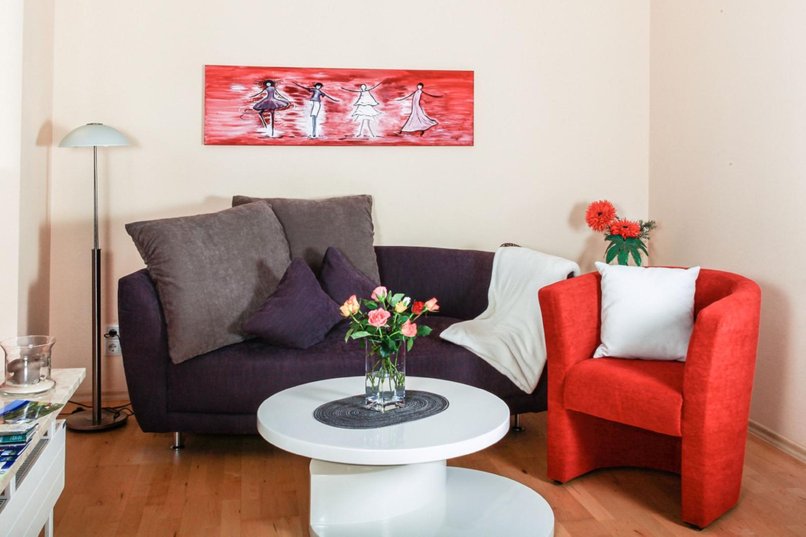 Ein Wohnzimmer mit Sofa, Sessel und Tisch. An der Wand hängt ein Bild.