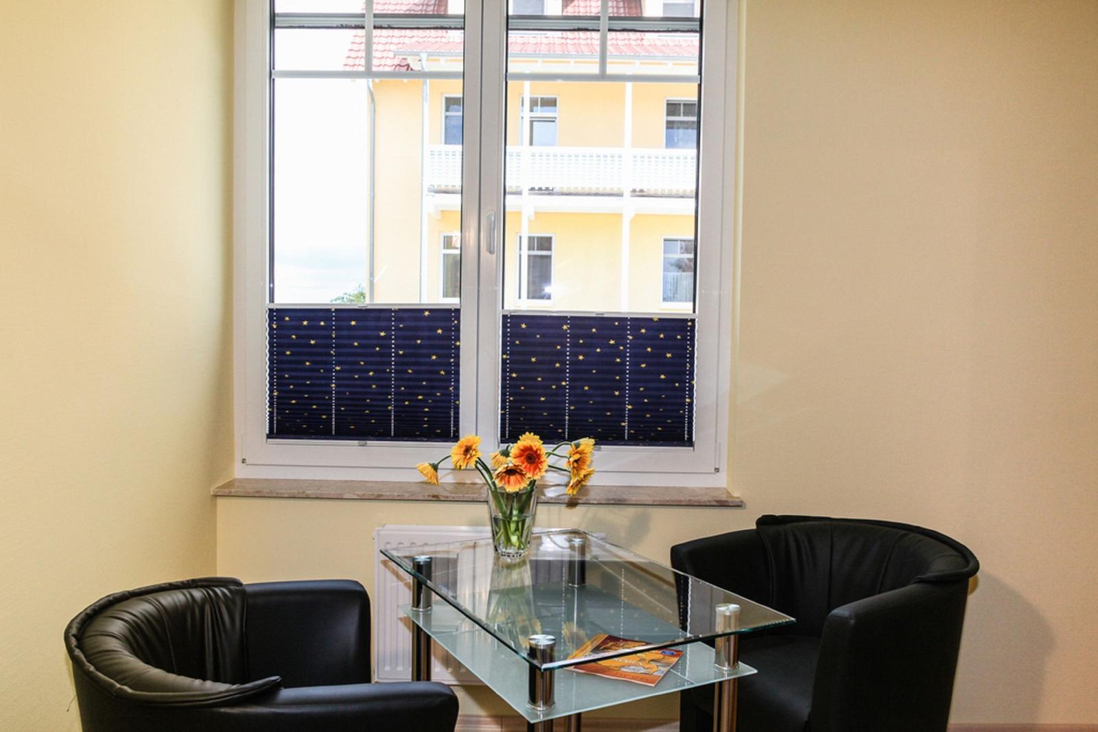 Zwei schwarze Sessel und ein Glas-Tisch stehen vor einem Fenster mit Sternen-Jalousien.