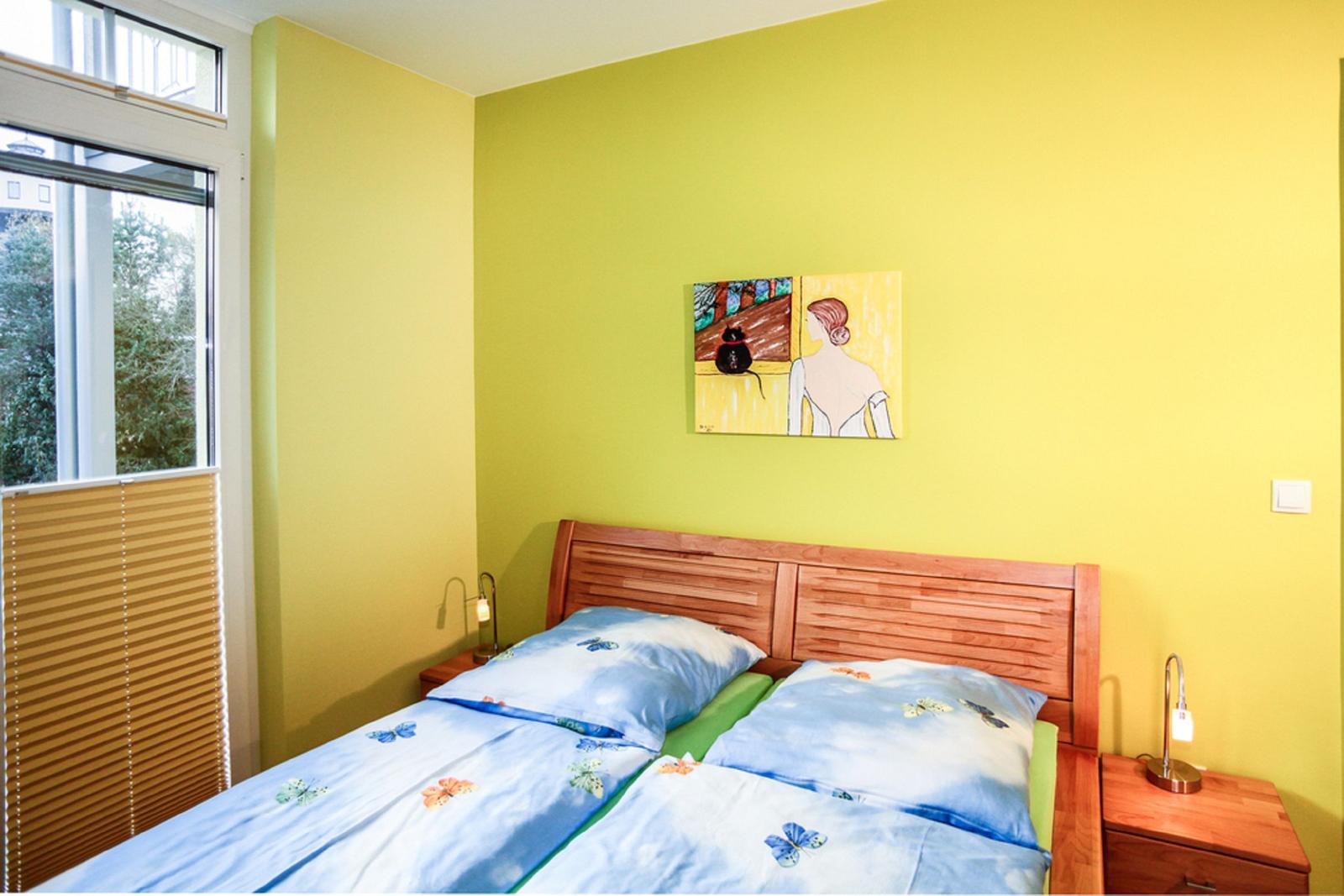 Schlafzimmer mit gelben Wänden, Bett mit blauer Bettwäsche und zwei Nachttischen.