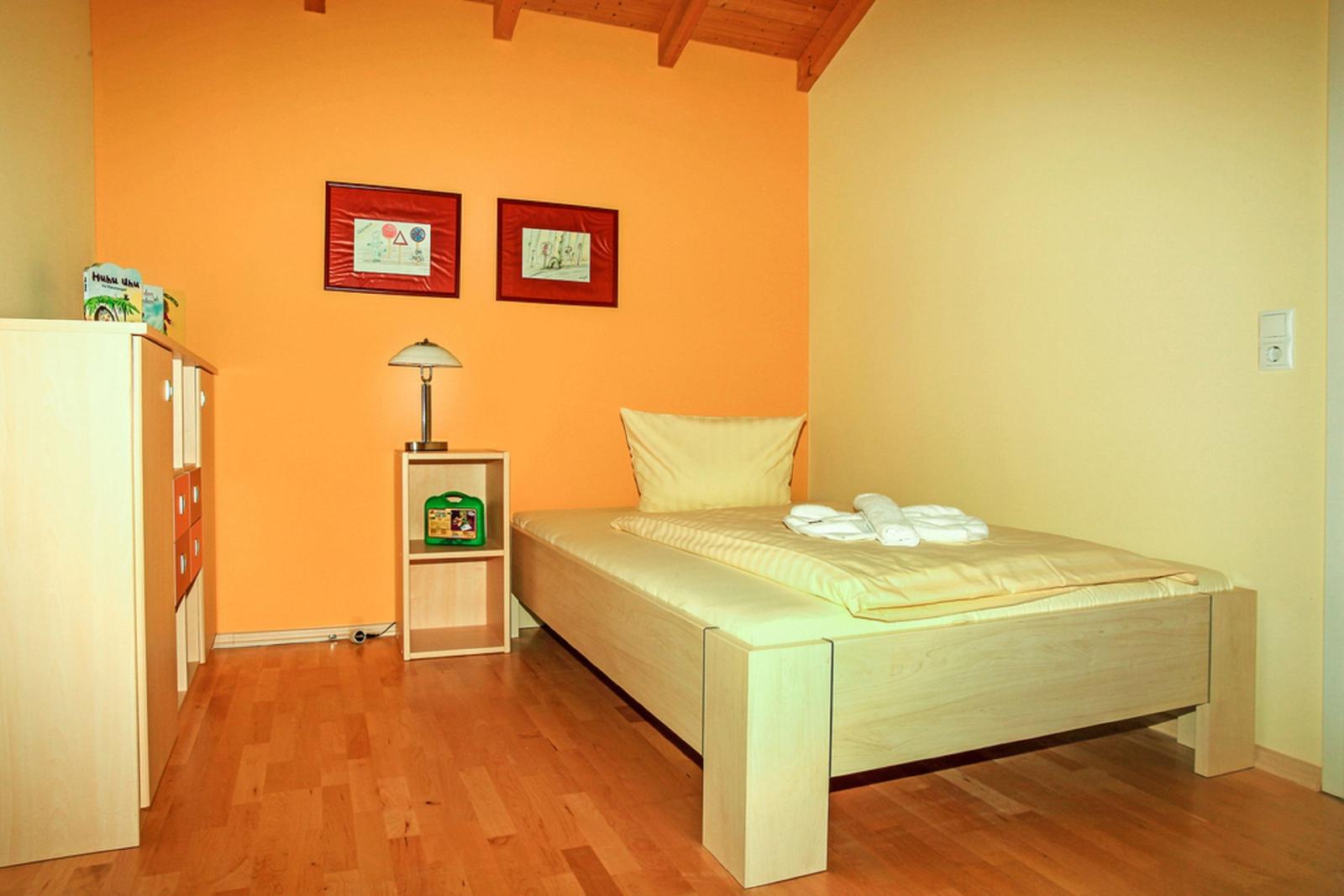 Ein Schlafzimmer mit Holzboden, Bett, Schrank und Nachttisch. Wandfarbe orange und gelb.