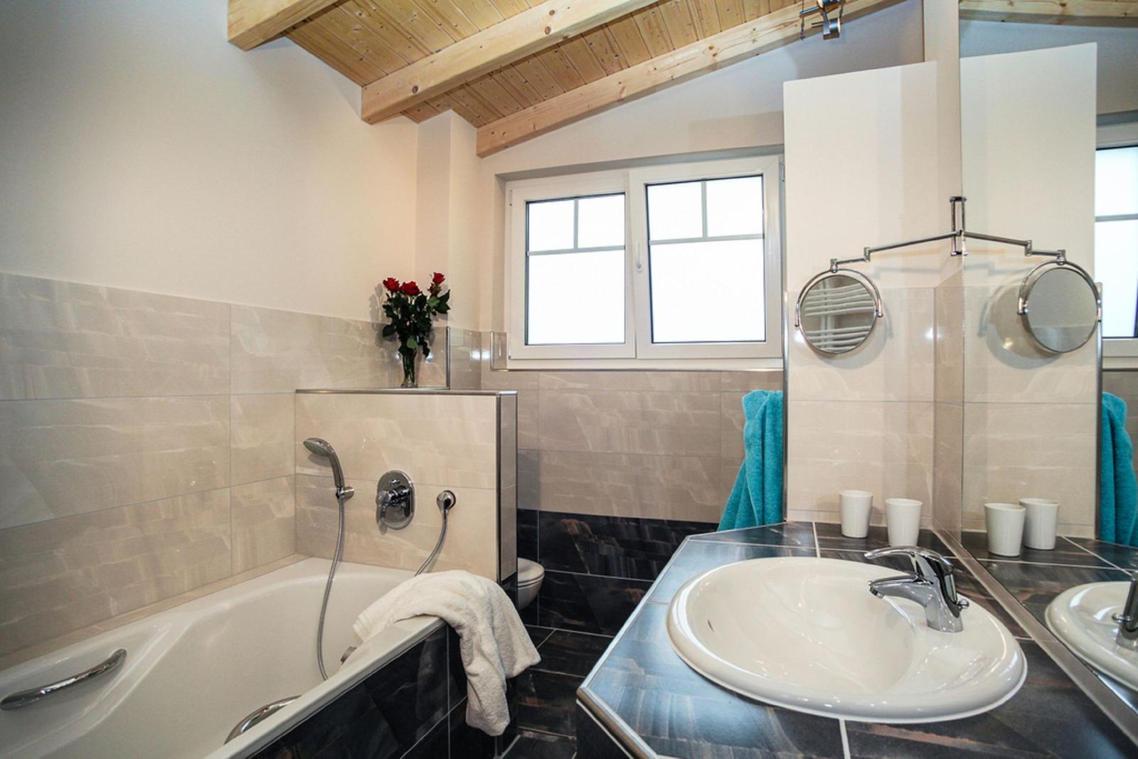 Bad mit Badewanne, Waschbecken und Fenster. Holzdecke und rote Rosen.