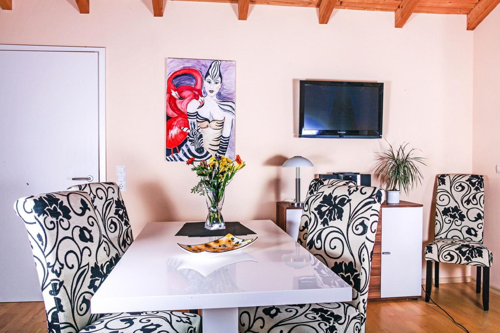 Esszimmer mit Tisch, Stühlen, Fernseher und Wandbild.