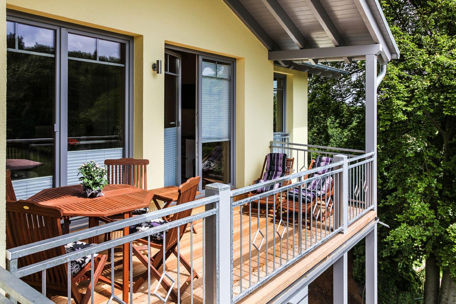 Terrasse mit Holztisch, Stühlen und Liegestühlen. Blick in den Wald.