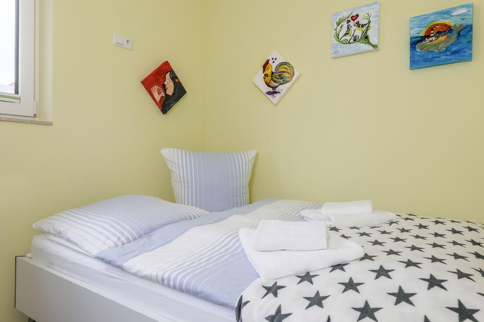 Ein Bett mit gestreifter Bettwäsche und einem Sternenbezug. An den Wänden hängen farbige Bilder.