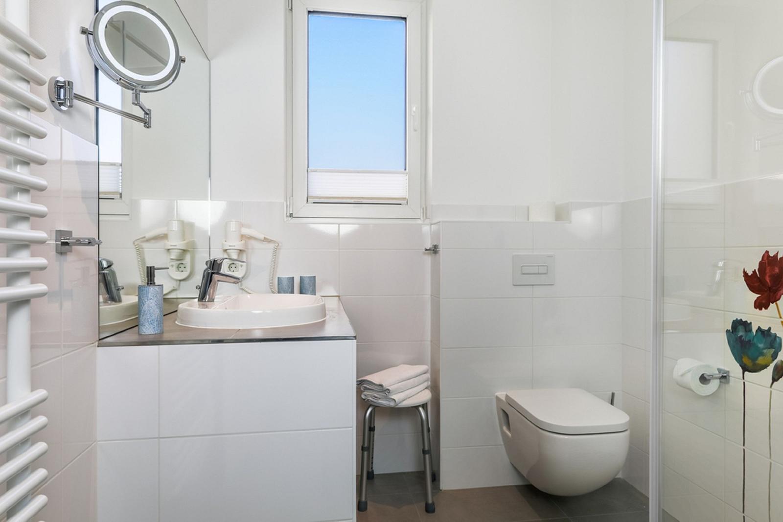 Badezimmer mit Dusche, Toilette, Waschbecken und Fenster.