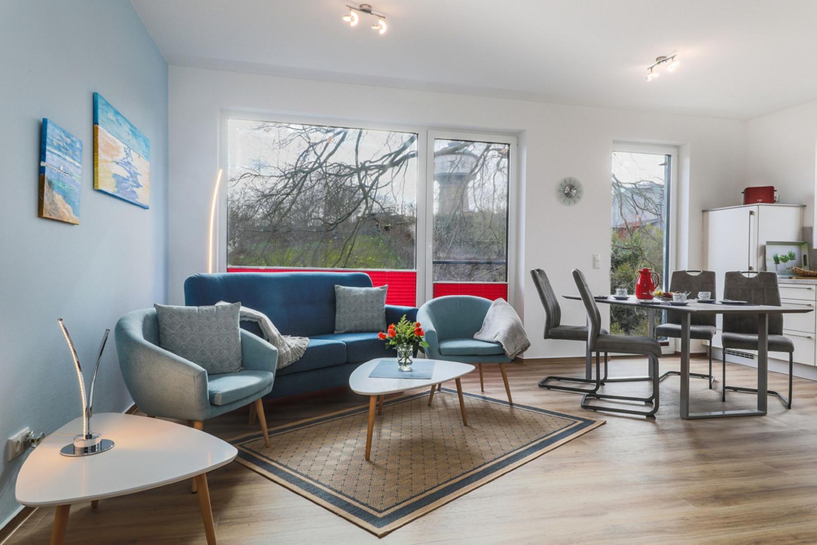 Wohn- und Essbereich mit Sofa, Sesseln und Tisch. Durchgänge zu Küche und Balkon.