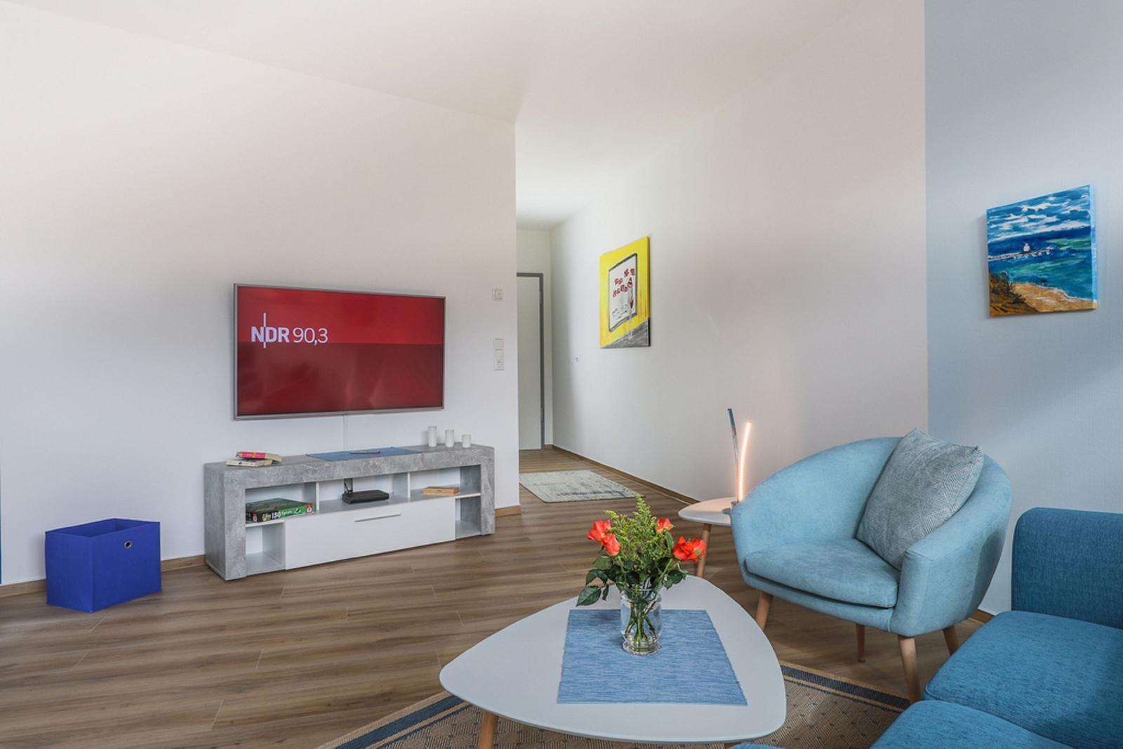 Wohnzimmer mit TV, Sitzgelegenheiten und dekorativen Wandbildern.