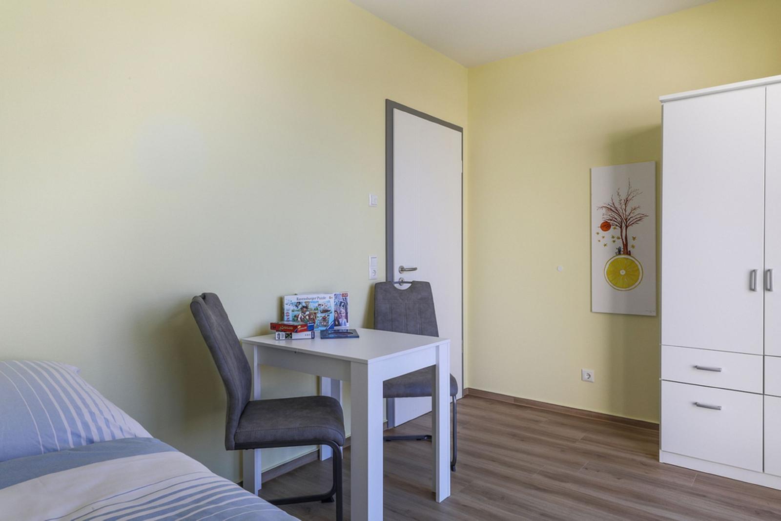 Ein Zimmer mit Bett, Schreibtisch, Stühlen und Kleiderschrank an der Wand.