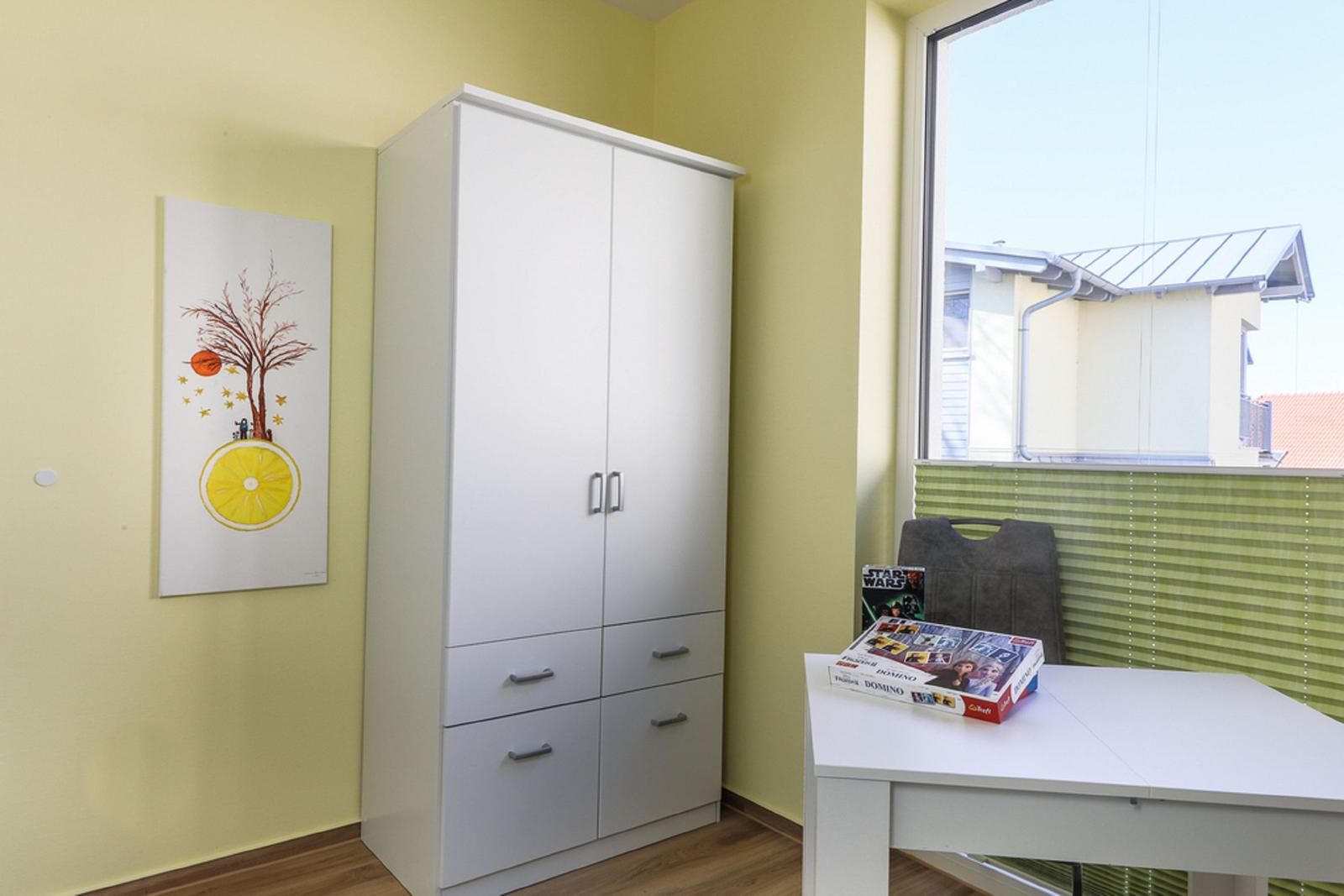 Ein Raum mit weißen Schränken, einem Tisch und einem Fenster mit grünen Jalousien.