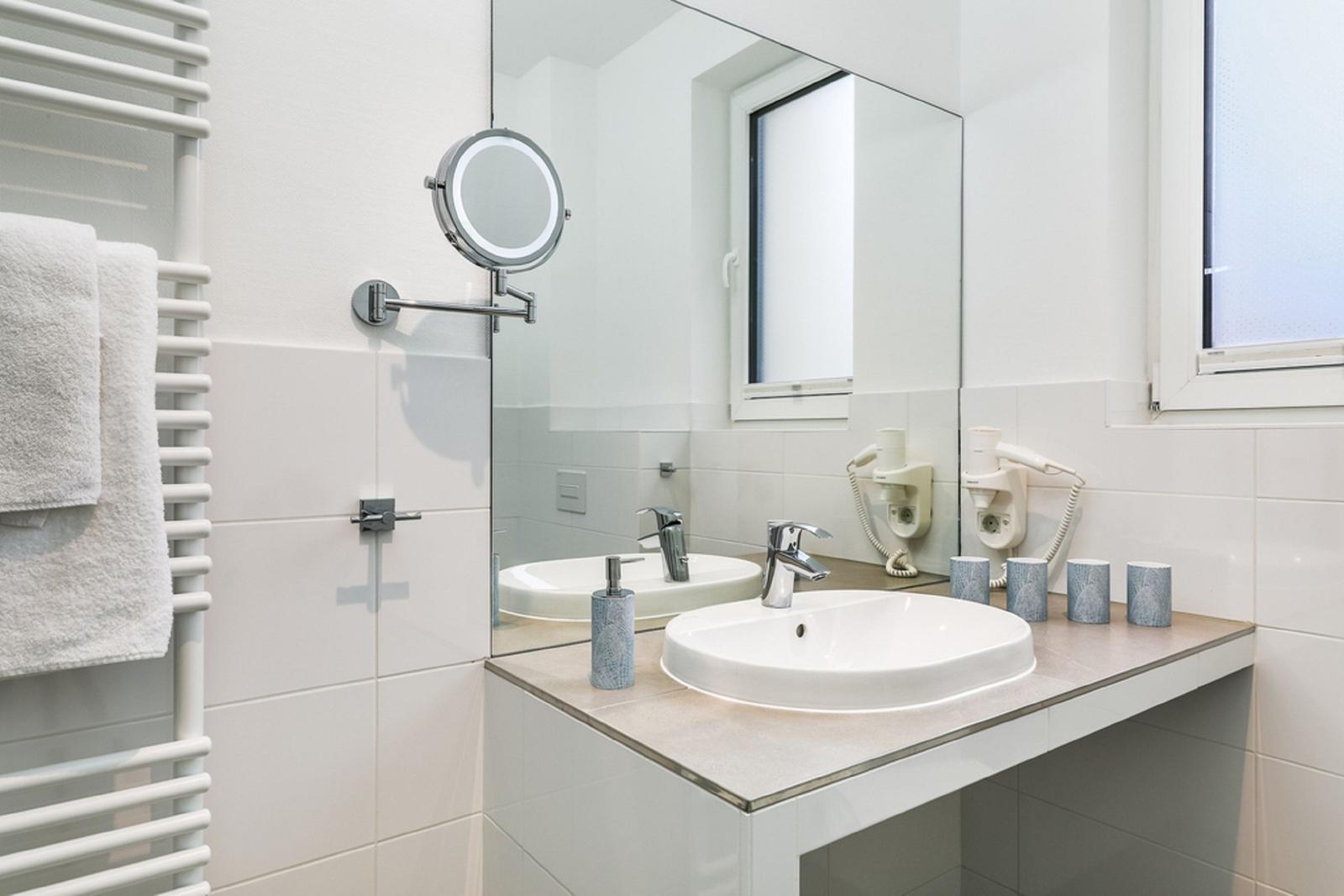 Badezimmer mit Waschbecken, Spiegel, Handtuchhalter und Fenster.