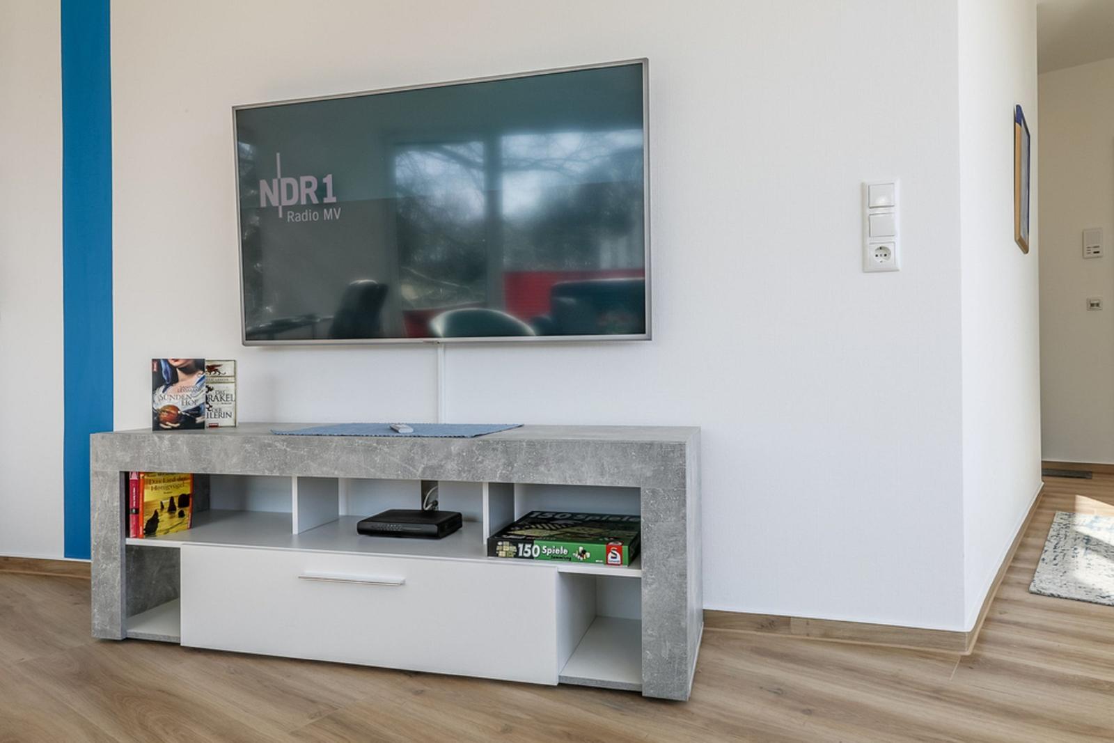 TV auf Wandhalterung, Unterputz mit Spielboxen und Buchern.