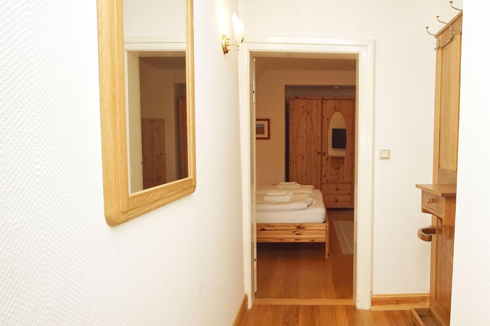Schlafzimmer mit Holzbett und Kleiderschrank über Flur mit Spiegel und Garderobe.