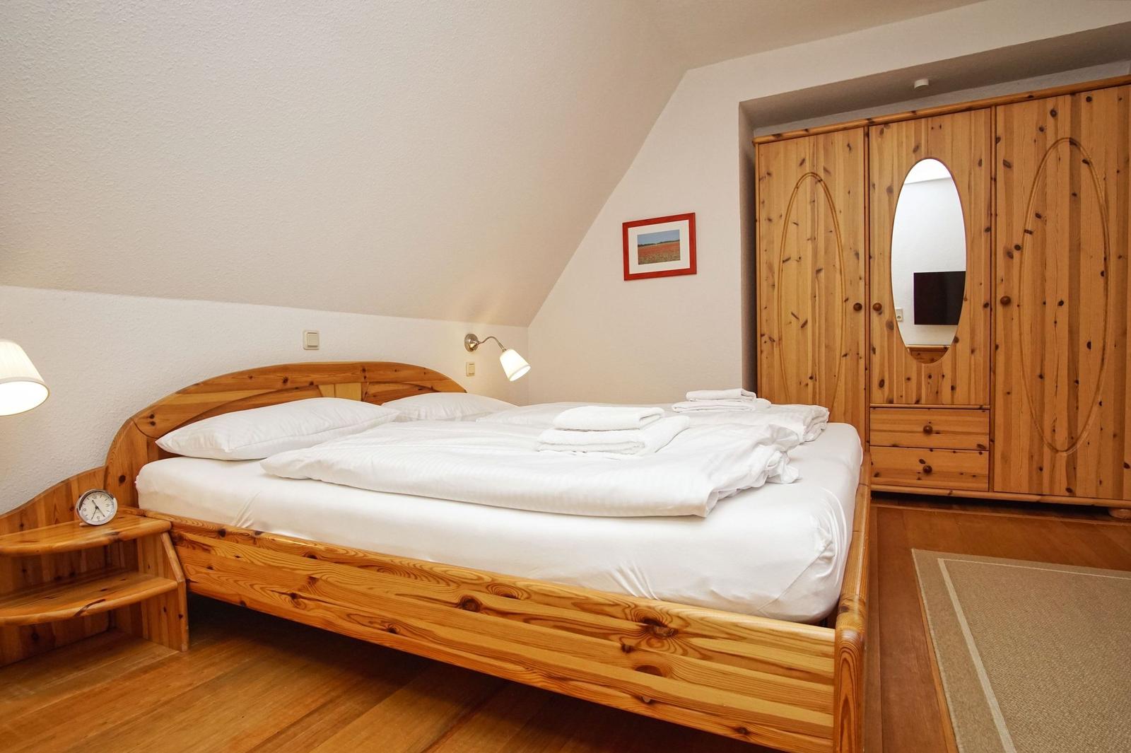 Schlafzimmer mit Holzbett, Kleiderschrank und Stehlampe.