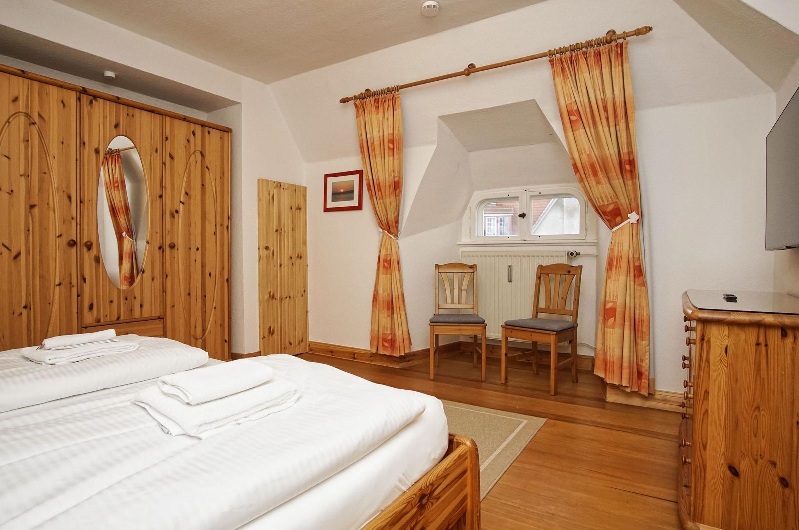 Schlafzimmer mit Holzbett, Kleiderschrank und Fenster mit Vorhängen.