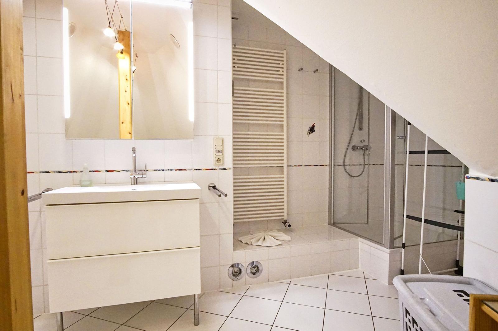Badezimmer mit Dusche, Waschbecken und Heizkörper unter Dachschrägen.