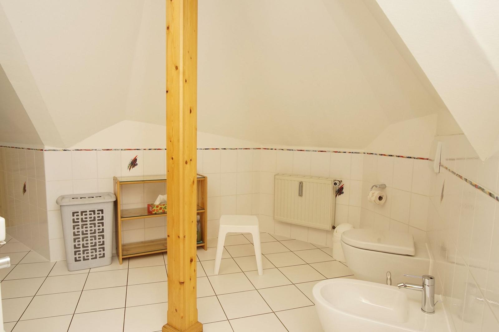 Badezimmer mit Toilette, Waschbecken und Duschbereich unter Dachschrägen.