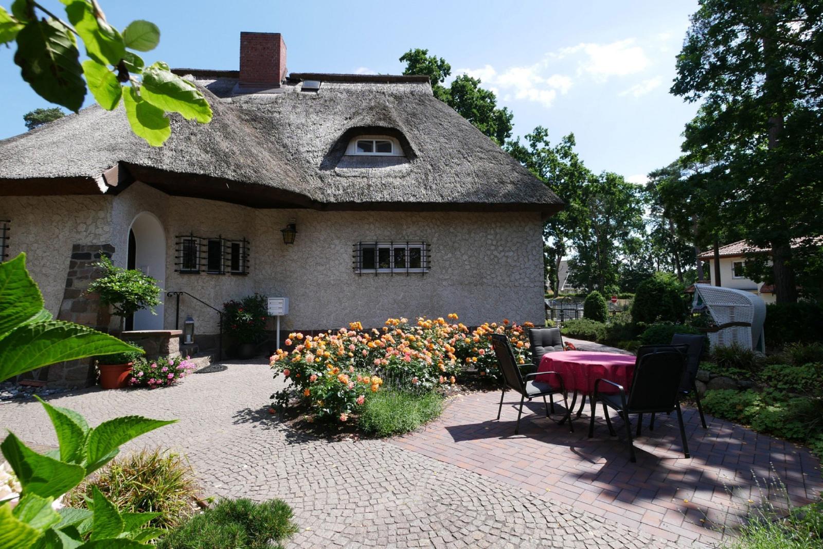 Haus mit Strohdach und Garten mit Tisch und Stühlen.