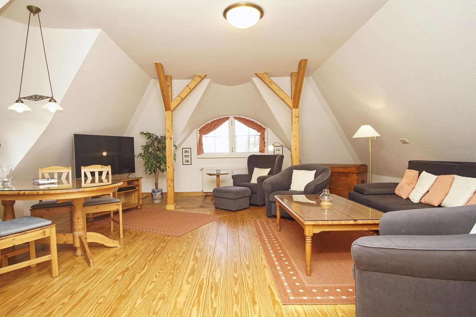 Wohn- und Essbereich mit Holzdielen, Sitzgruppe und Fernseher unter schrägen Dachbalken.