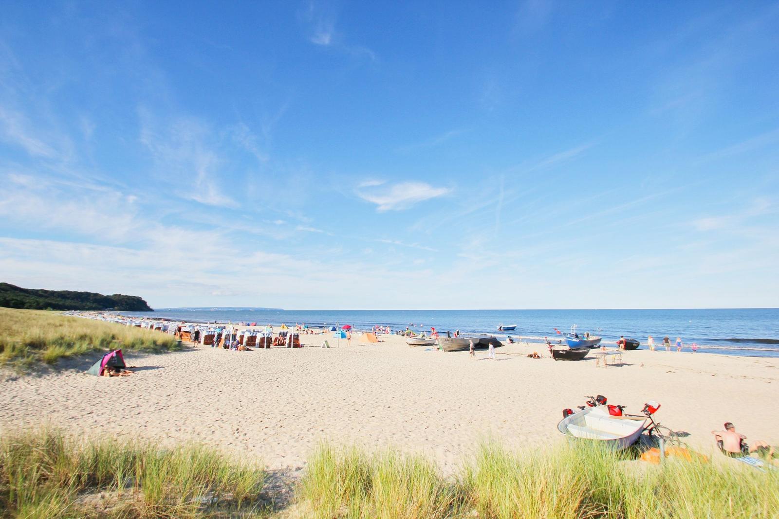 Strand mit Sand, Booten und Strandkörben unter blauem Himmel.