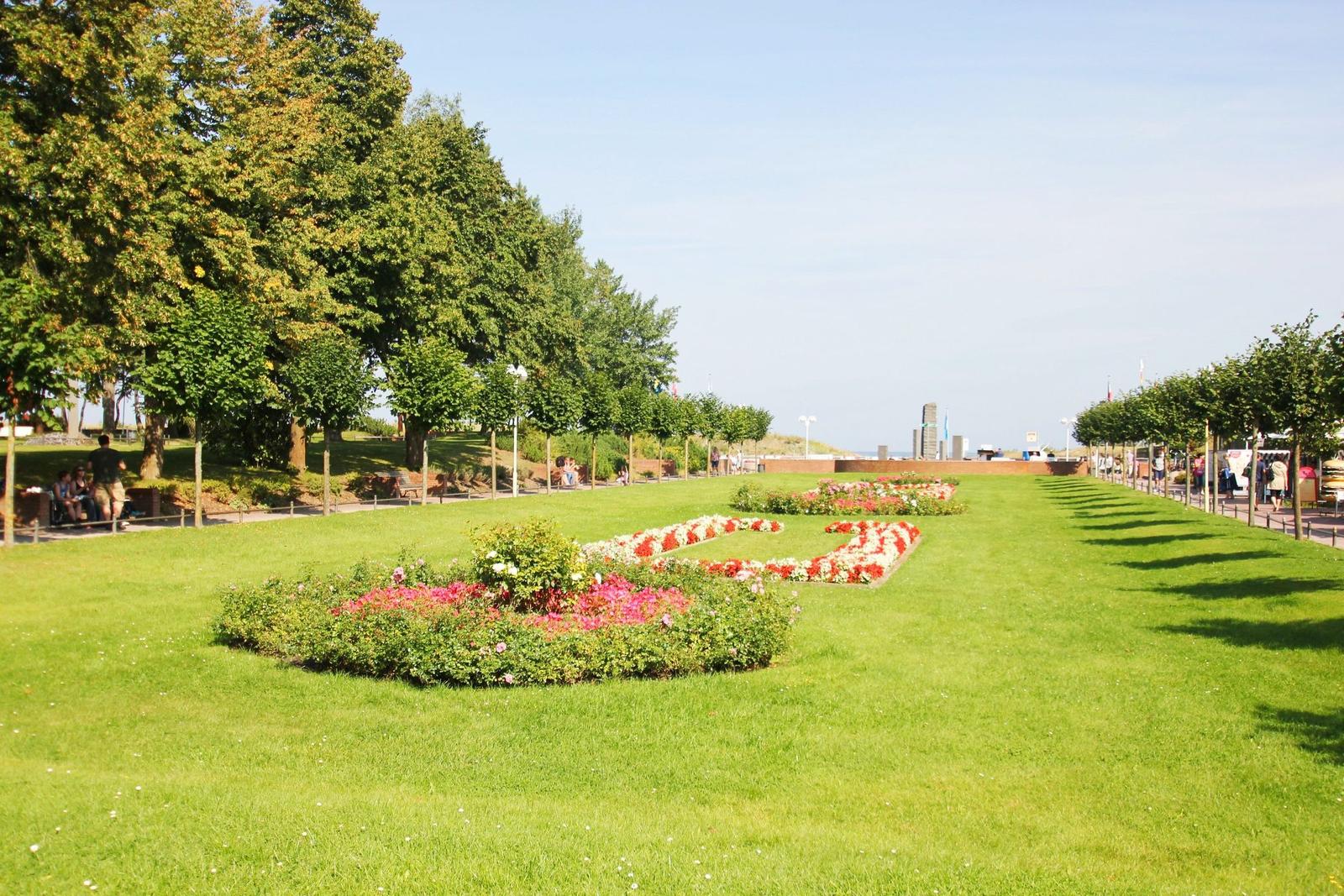 Grünflächen mit Blumenbeeten und Bäumen entlang eines Weges.