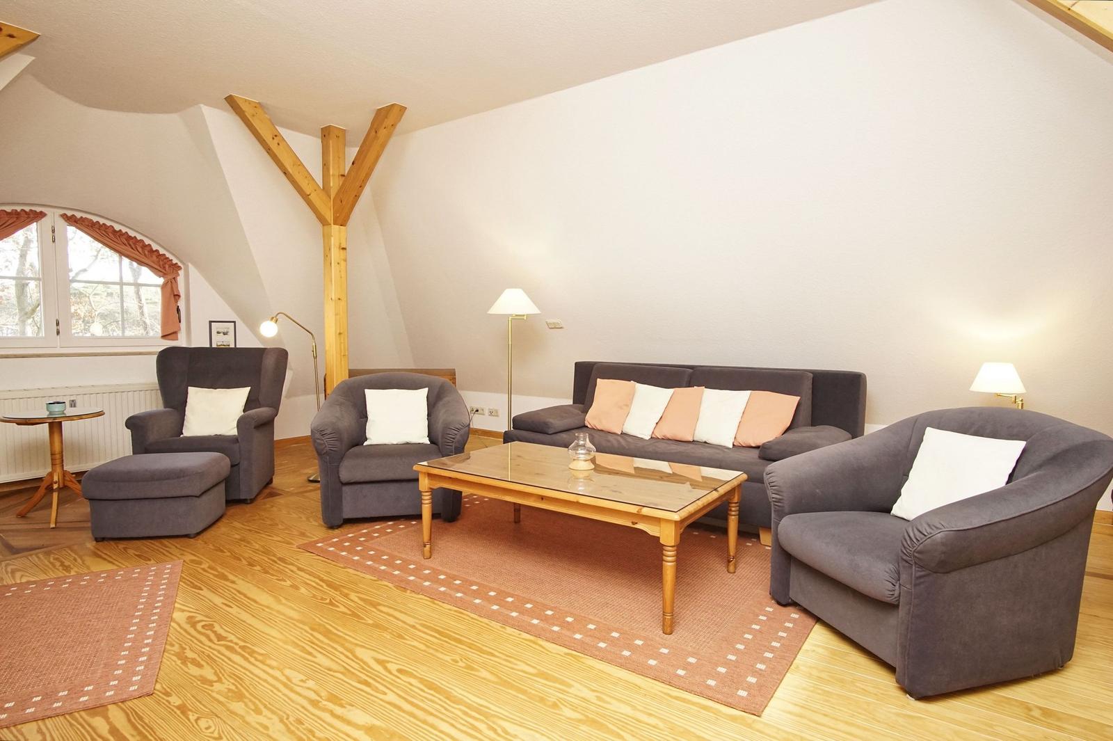 Wohnzimmer mit grauen Sesseln, Sofa und Holztisch. Holzdecke und Fenster mit Vorhängen.