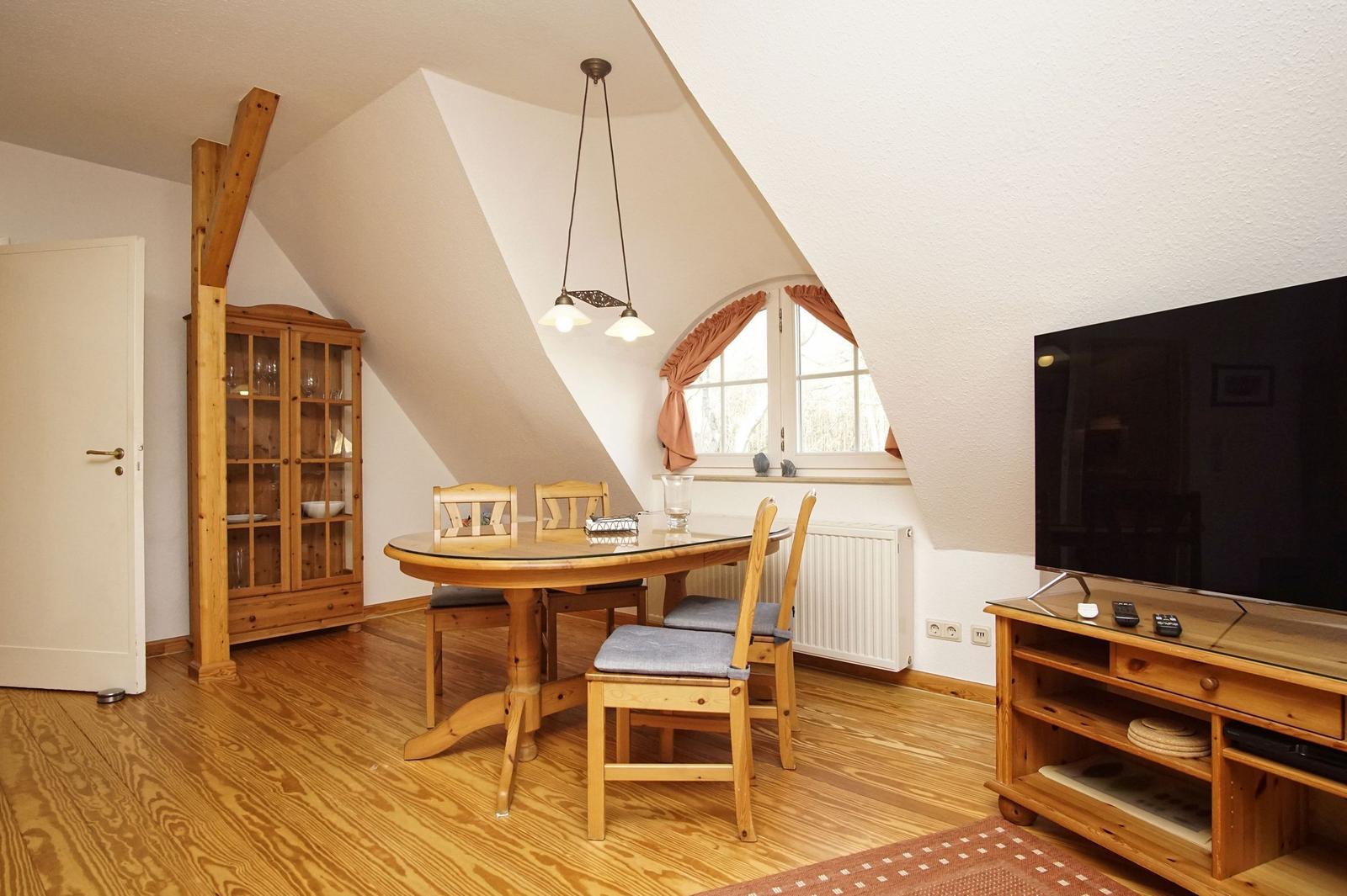 Esszimmer mit Holztisch, Stühlen und TV-Schrank unter schrägem Dach