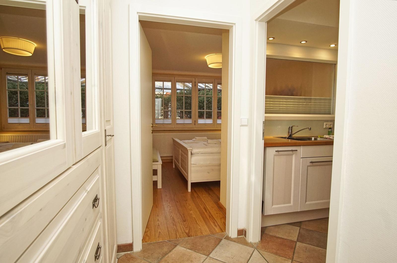 Durchgang zu Schlafzimmer und Küche mit Holzboden und weißen Möbeln.