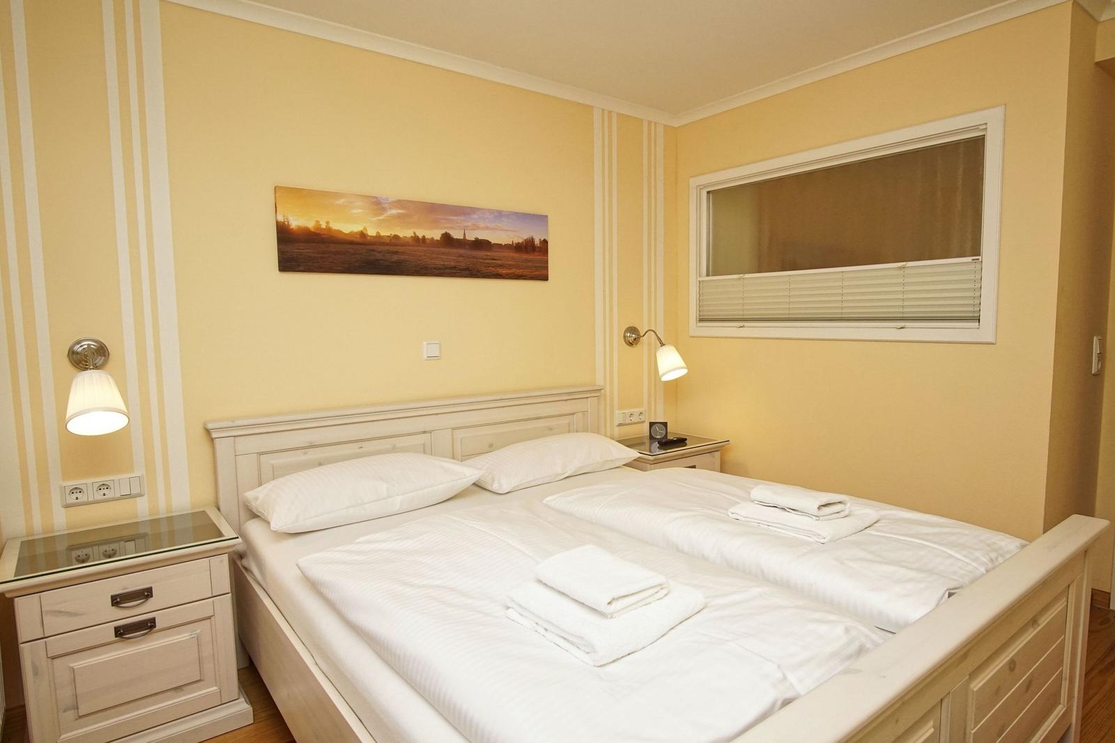 Schlafzimmer mit Doppelbett, Nachttischen und Wandbild. Fenster mit Jalousie.