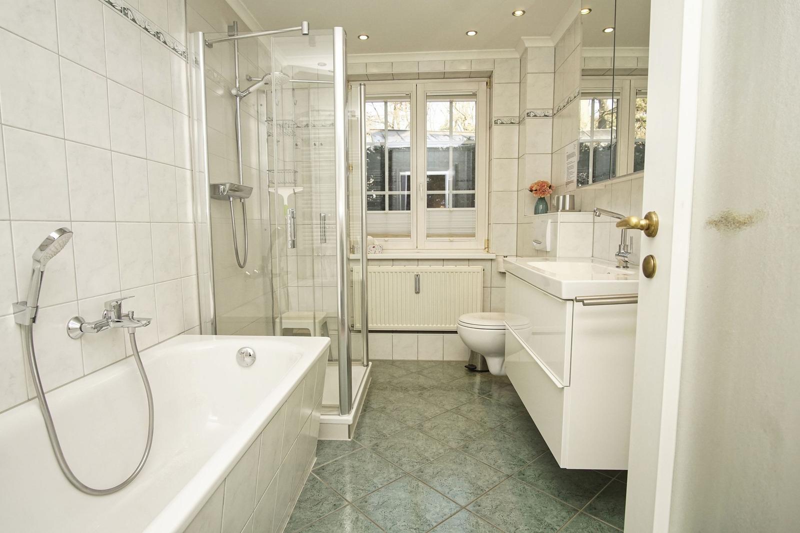 Badezimmer mit Badewanne, Dusche, Waschbecken und Toilette. Fenster mit Blick nach draußen.