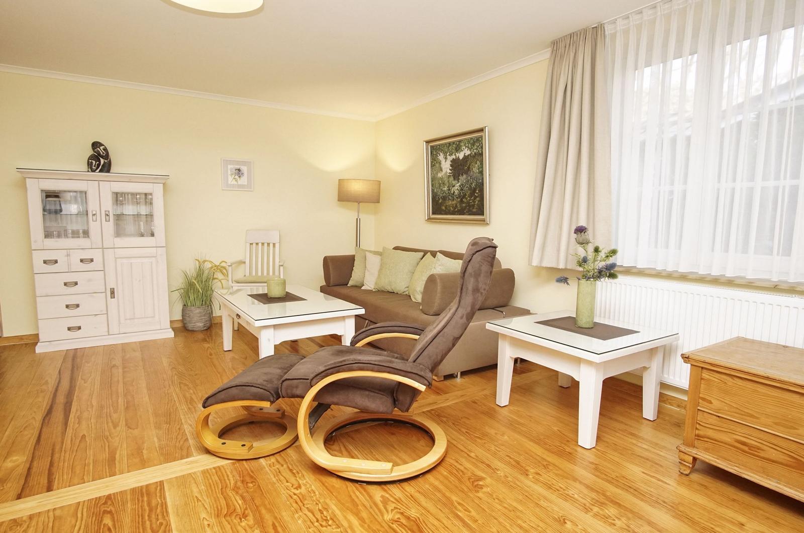 Wohnzimmer mit braunem Sofa, weißem Tisch und Holzboden. Fenster mit weißen Vorhängen.