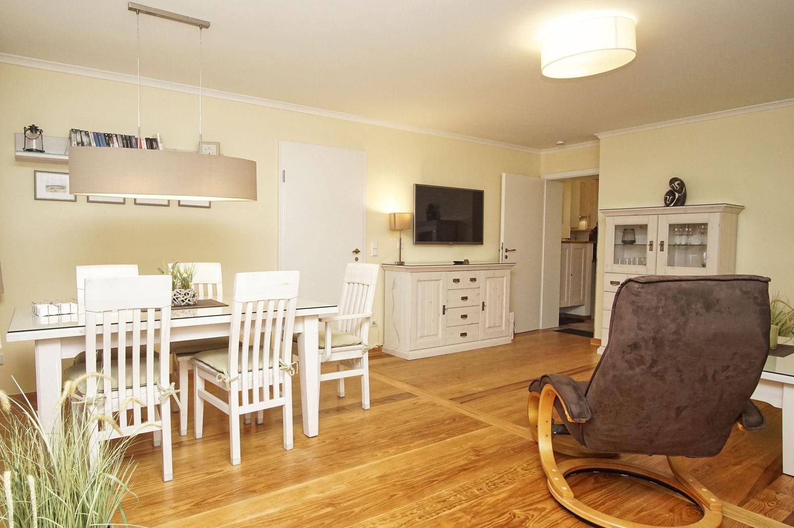 Essbereich mit weißem Tisch und Stühlen, Fernseher und Schaukelsessel im Wohnbereich.