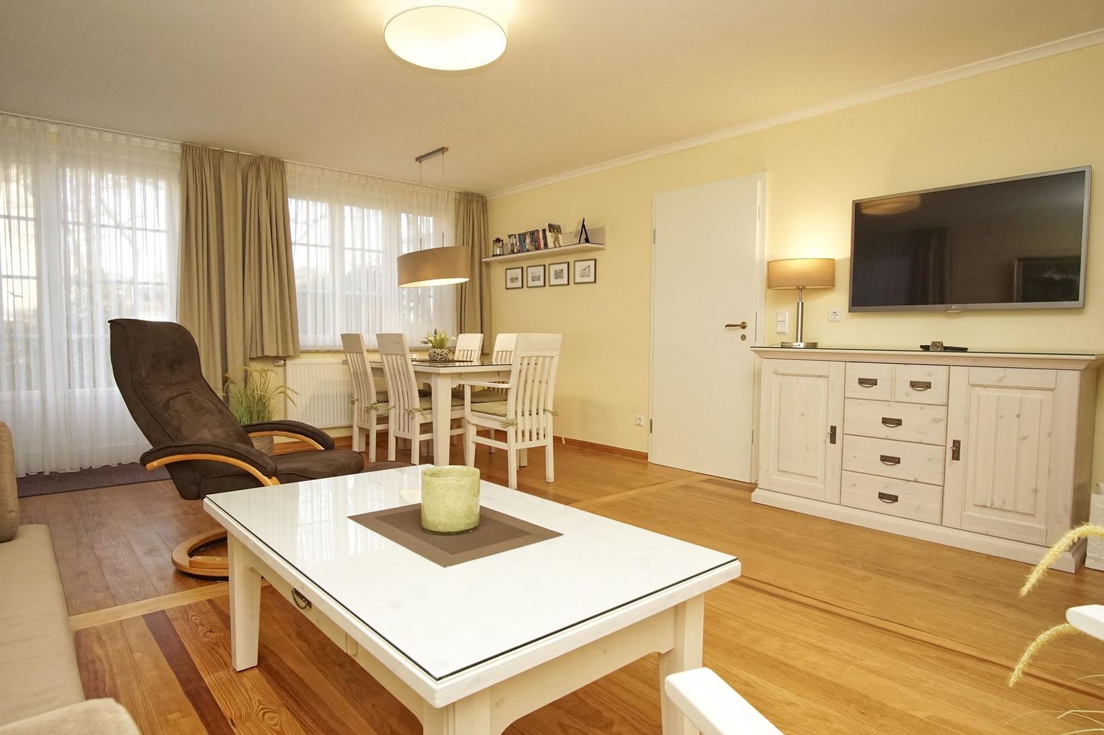 Wohn- und Essbereich mit Holzboden, TV, Esstisch und Sessel.