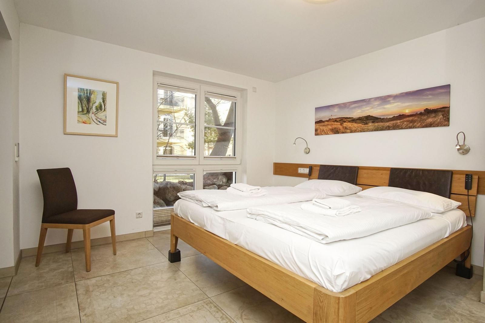 Schlafzimmer mit Bett, Stuhl und Fenster. Wandbilder und Beleuchtung.