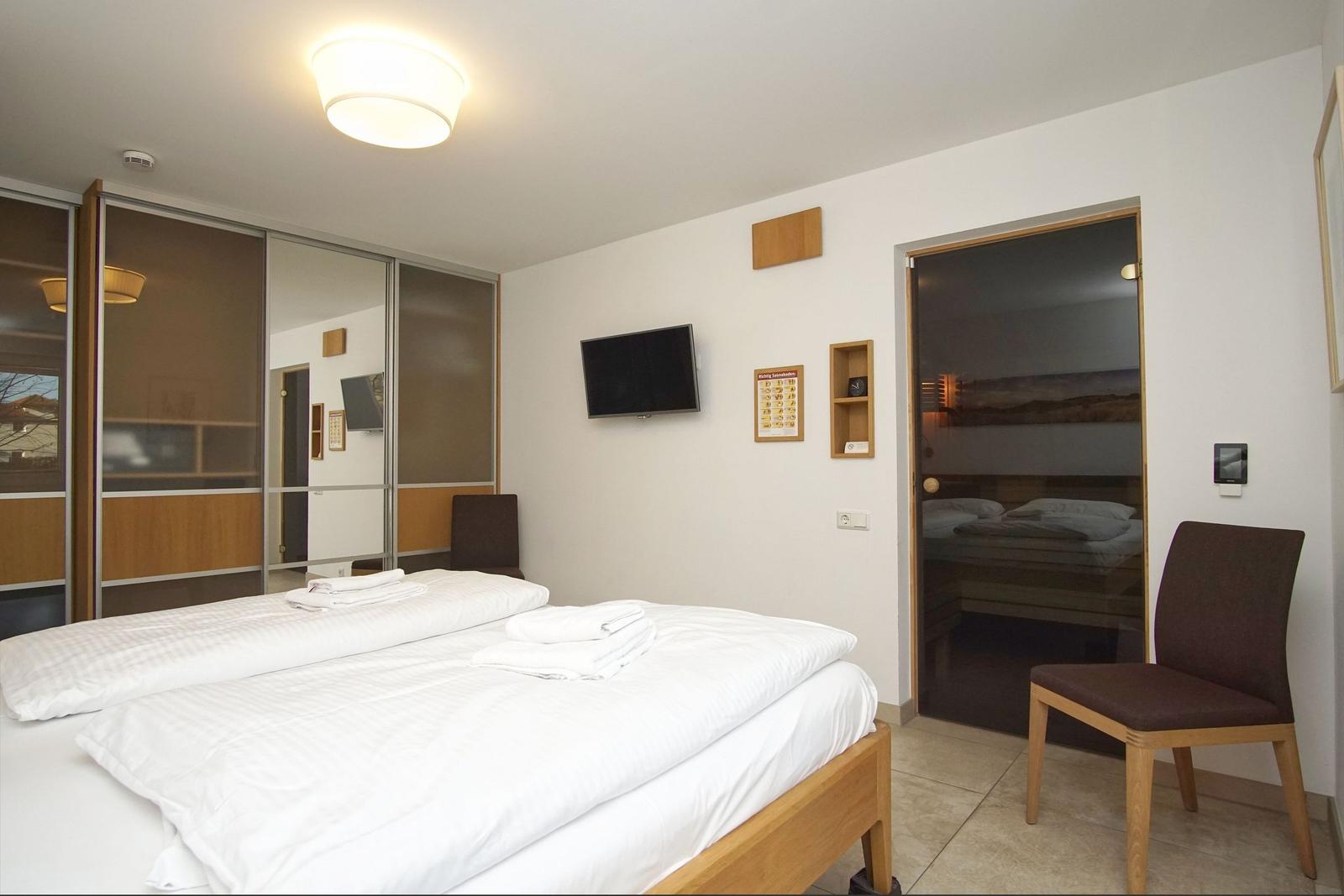 Zimmer mit Doppelbett, TV und Sitzgelegenheit. Sauna ist im Anschluss.