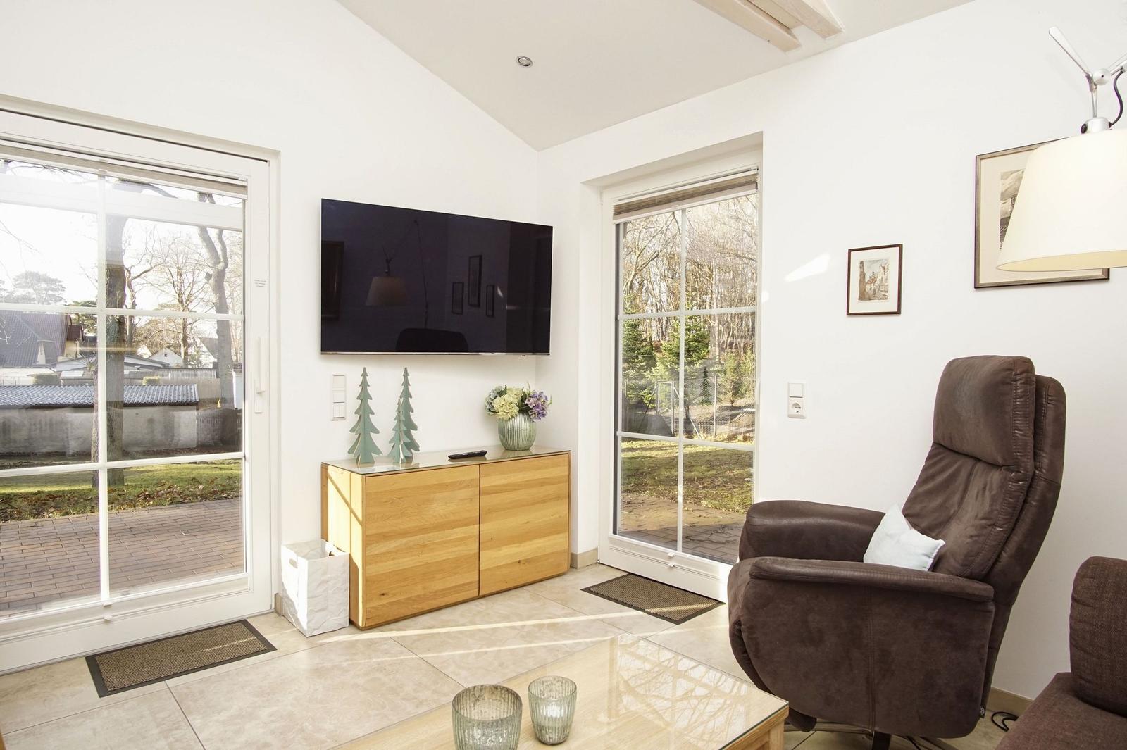 Wohnzimmer mit Fernseher, braunem Sessel und Glasfronten zur Außenterrasse.