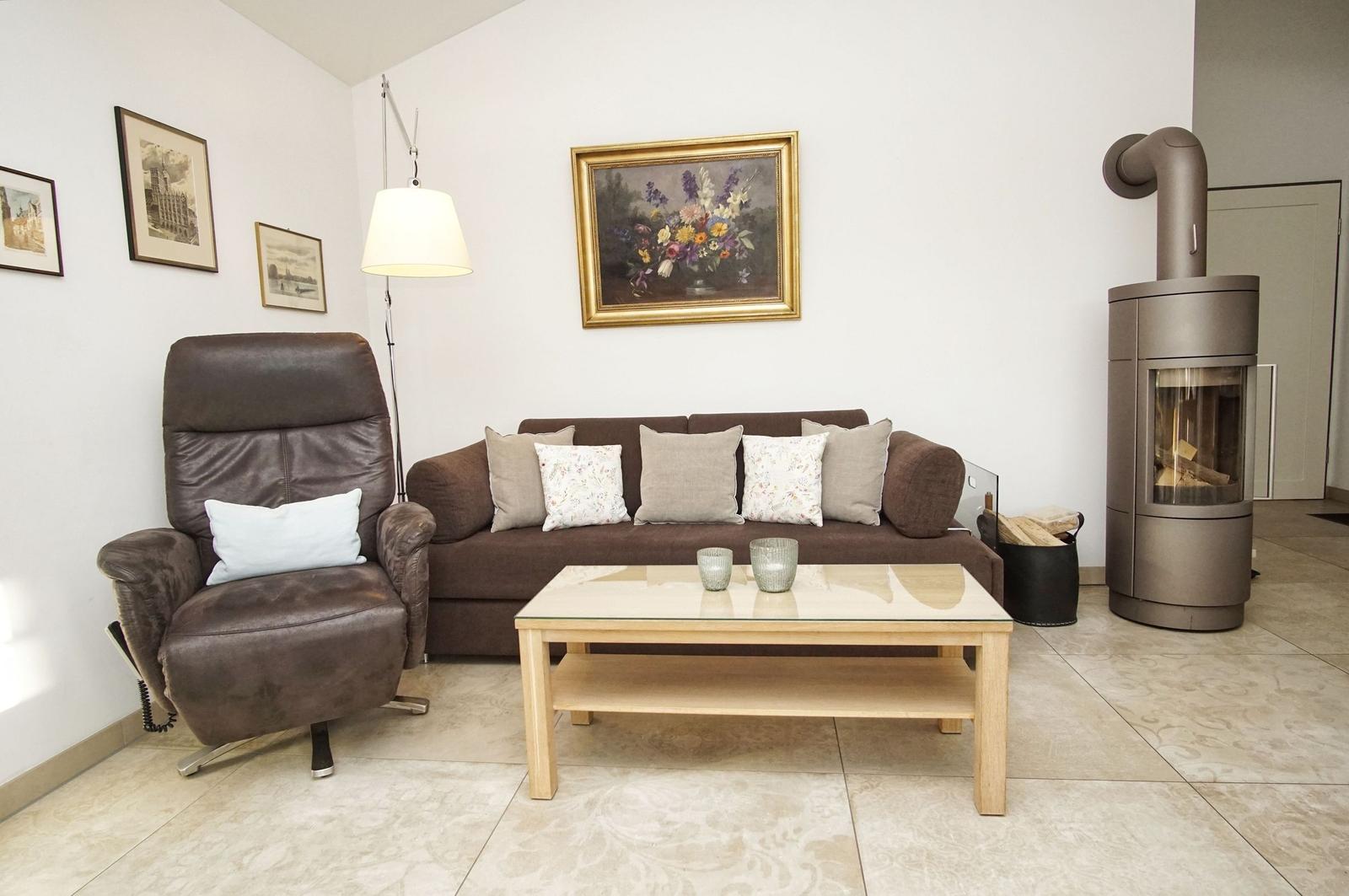 Wohnzimmer mit Sofa, Sessel, Tisch und Kaminofen.